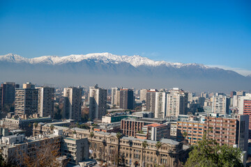 Distant snow-capped Andes mountain range beyond urban skyline.