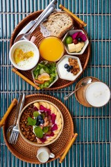 A delicious vegetarian breakfast bowl of fruits and granola with a set of various healthy food in wickerwork trays on blue tile background