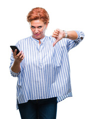 Atrractive senior caucasian redhead woman texting using smartphone over isolated background with angry face, negative sign showing dislike with thumbs down, rejection concept