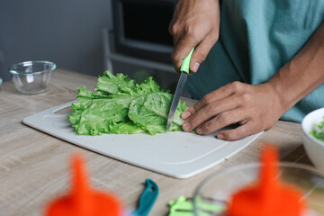 Man making salad, cut the lettuce leaves and put it into a bowl at the kitchen
