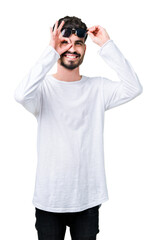 Fototapeta premium Young handsome man wearing sunglasses over isolated background doing ok gesture with hand smiling, eye looking through fingers with happy face.