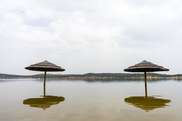 Straw sunshades submerged in water at Azenhas Del’Rei beach, Alqueva Dam, nearly at full capacity due to heavy winter rains.
