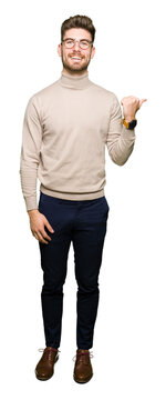 Young handsome business man wearing glasses smiling with happy face looking and pointing to the side with thumb up.