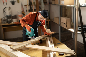 Female carpenter using a jigsaw to cut wood in her workshop, demonstrating precision and craftsmanship in woodworking projects.