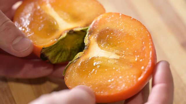 Persimmon cut into two parts on the table. Taking juicy ripe persimmon fruit, eating exotic healthy fruits