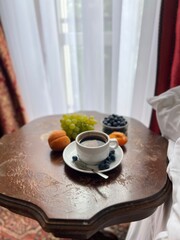 Cup of coffee with fresh fruits on the bedside table in a hotel room with red curtains 