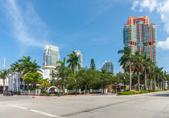 Lush trees and palms on city corner with high-rise buildings and blue sky background.