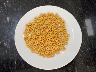 White bowl filled with crunchy cereal rings on a dark marble countertop