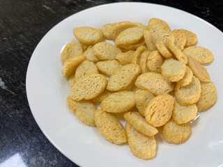 Crispy, golden-brown bread chips on a white plate against a dark marble background.