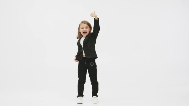 Concept of business, deal and modern technology. Little business girl on a white background in the studio presses her mobile phone and shows a &ldquo;super&rdquo; gesture of approval.