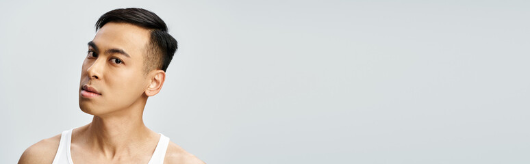 Obraz premium Handsome Asian man in white tank top posing in grey studio setting, banner