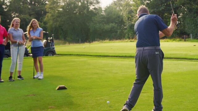 Mature and mid adult couples playing round of golf together watching man make tee shot - shot in slow motion