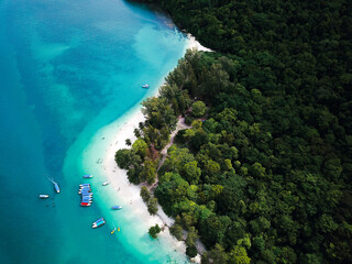 Aerial view of Perhentian Islands beach with boats docked near a wooden pier and lush greenery