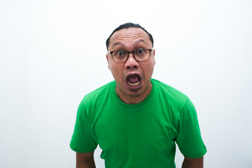 Fototapeta premium Shocked Asian man in green t-shirt, wide-eyed with surprised expression, humorous