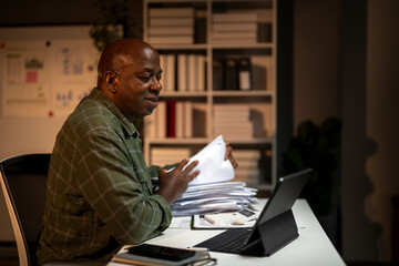 Fototapeta premium A man is sitting at a desk with a laptop and a stack of papers