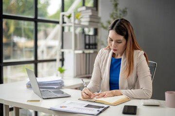 Obraz premium A woman is sitting at a desk with a laptop and a notebook