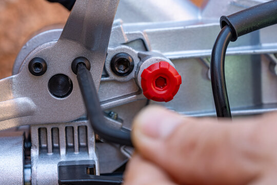 A man unscrews the bolt with a hex wrench for adjusting the miter saw, closeup. Worker with allen screw with his wrench
