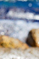 Sea waves rolling and crashing on the rocks with lots of white bokeh spots of sun glare on the...