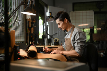 Side view of professional artisan is meticulously measuring and cutting a large piece of leather on...