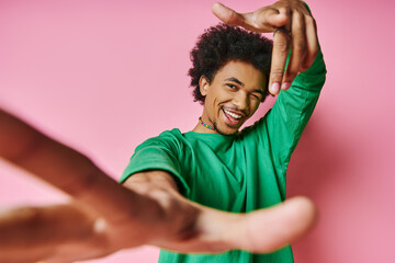 A joyful African American man, curly hair in a green shirt, dances energetically on a vibrant pink...