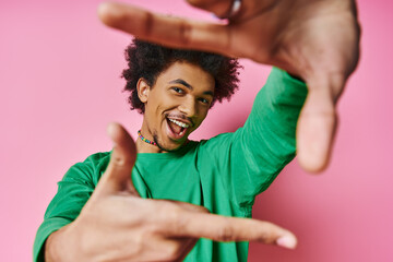 A cheerful young African American man in casual wear on a pink background makes a gesture with his...