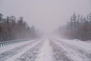 Snow-covered highway through forest during intense winter storm in daytime