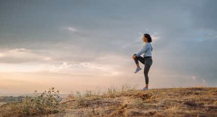 An athletic woman is exercising on a hill at sunset, embracing the tranquil surroundings