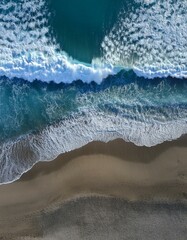 Fototapeta premium Drohnenaufnahme oder Vogelperspektive eines wunderschönen, transparenten, klaren Meeres oder Ozeans mit Wellen und Gischt, die auf den dunkelblauen oder grauen Sandstrand schlagen.