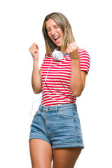 Young beautiful woman listening music wearing headphones over isolated background very happy and excited doing winner gesture with arms raised, smiling and screaming for success. Celebration concept.