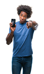 Afro american man holding broken smartphone over isolated background pointing with finger to the...