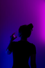 Silhouette of a girl drinking from a glass. Dark profile of mysterious girl drinking from a glass on colored background.