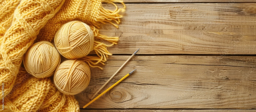 Poster top view of light yellow knitting wool needles knitted fabric and yarn on a wooden surface with copy