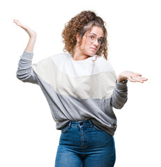 Beautiful brunette curly hair young girl wearing glasses over isolated background clueless and...