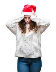 Young brunette girl wearing christmas hat over isolated background suffering from headache desperate and stressed because pain and migraine. Hands on head.