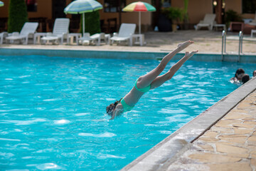 Girl jumping and diving into swimming pool on sunny day