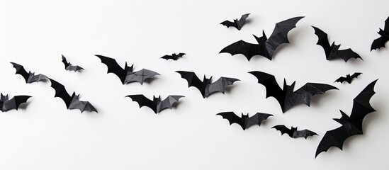 Fototapeta premium Black paper bats flying over a white background adding spooky flair to a Halloween and decoration concept with a copy space image