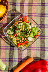Fresh vegan salad on kitchen table with cucumber, letuce, tomato, jellow pepper and chick peas, top view, flat lay