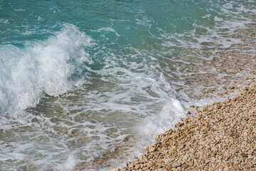 Beautiful pebbles beach with waves and blue sky. Relaxing aerial scene, summer vacation. Holiday template banner. Waves surf with amazing blue ocean lagoon, sea shore, coastline. Copy space.