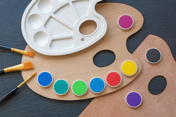 Palettes, paints,  and paintbrushes on black table. Flat lay, copy space