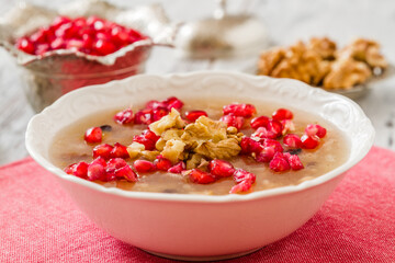 Traditional Turkish Ashura dessert garnished with pomegranate and walnuts served in a white bowl on a rustic wooden surface.