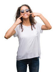 Young hispanic woman wearing sunglasses smiling confident showing and pointing with fingers teeth and mouth. Health concept.