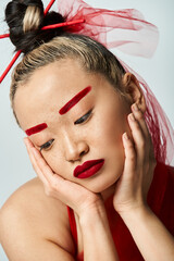 Asian woman in vibrant red dress, hands on face.
