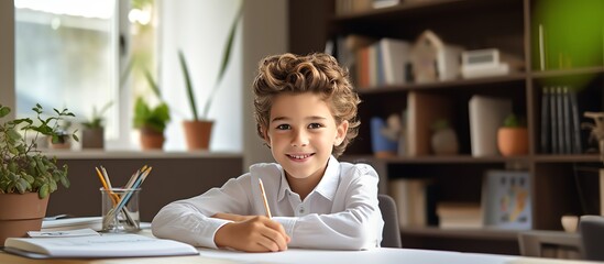 Happy school boy writing at a desk, looking at the camera and smiling while doing homework in the style of a modern home office room with white shelves