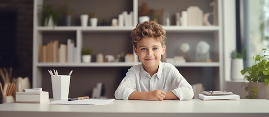 Happy school boy writing at a desk, looking at the camera and smiling while doing homework in the style of a modern home office room with white shelves