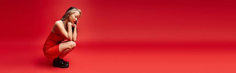 A vibrant Asian woman in a red dress sitting gracefully on a red floor.