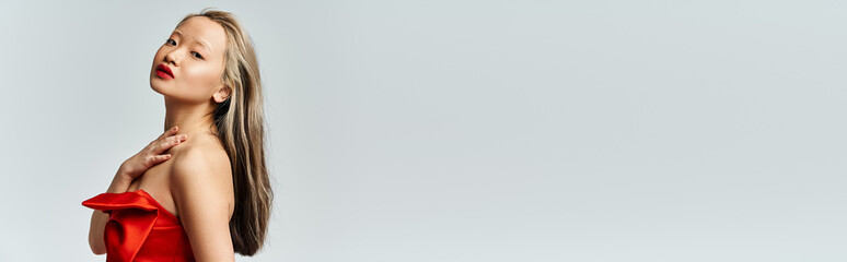 A graceful Asian woman is energetically posing in a striking red dress.