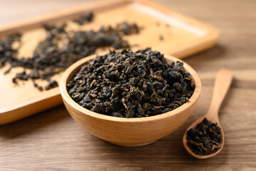 Dried Oolong tea leaves in bowl and spoon on wooden background