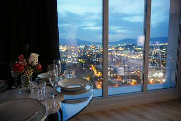 Fototapeta premium Romantic dining table setting next to window with night city view in a luxury apartment hotel room
