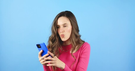 Attractive brunette woman look surprised wow hold mobile cell phone on blue background. Girl look on smartphone and doing sh gesture. Girl just found out big win news, wow, mobile phone victory.