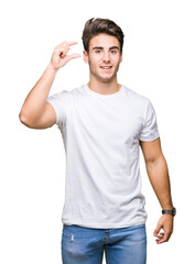 Young handsome man wearing white t-shirt over isolated background smiling and confident gesturing with hand doing size sign with fingers while looking and the camera. Measure concept.